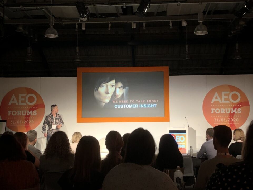 Speaker presenting on customer insight at the AEO Forum with an audience in attendance.