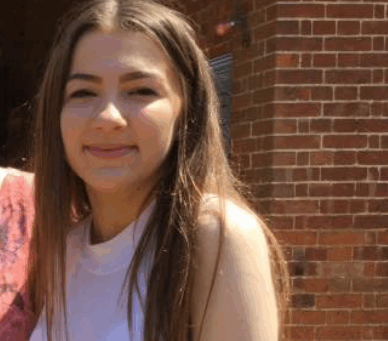 A young woman with long hair wearing a sleeveless top, smiling at the camera.