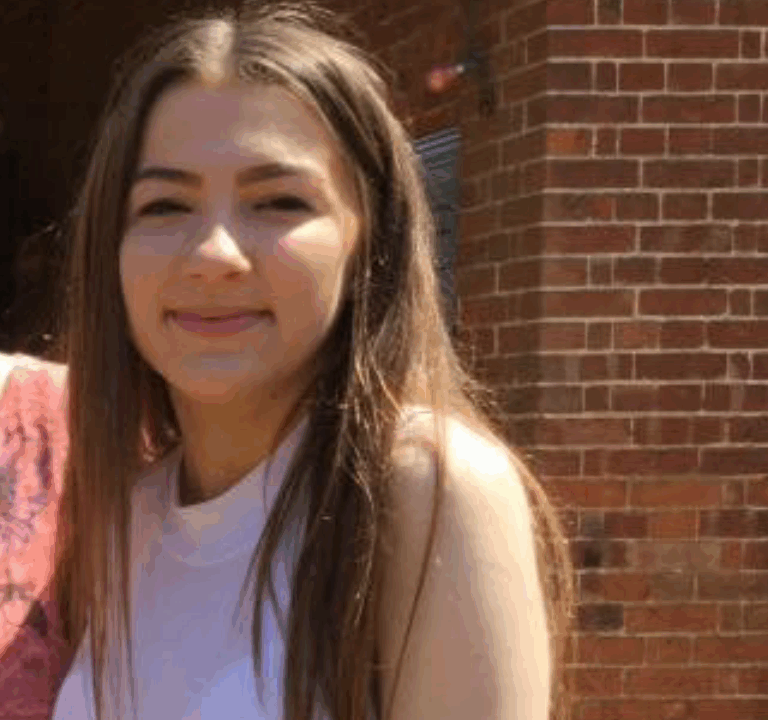 A young woman with long hair wearing a sleeveless top, smiling at the camera.