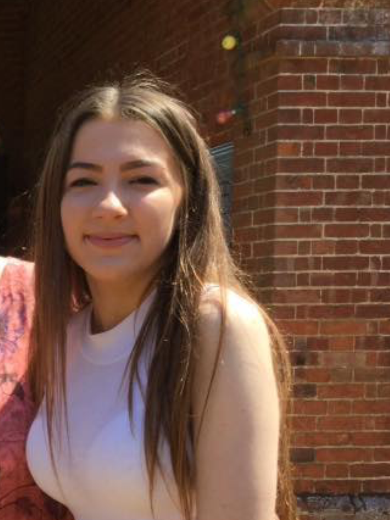 A young woman with long hair wearing a sleeveless top, smiling at the camera.