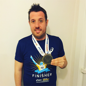 Man wearing a blue t-shirt holding a finisher medal with a ribbon.