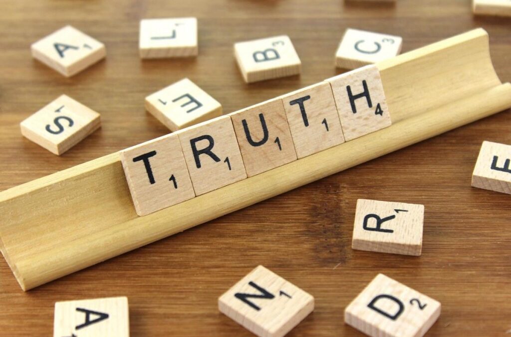Scrabble tiles arranged to spell the word 'TRUTH' on a wooden surface.