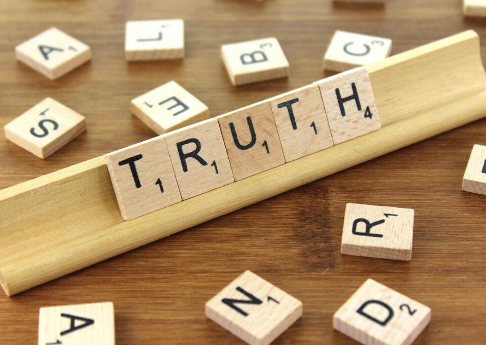 Scrabble tiles arranged to spell the word 'TRUTH' on a wooden surface.